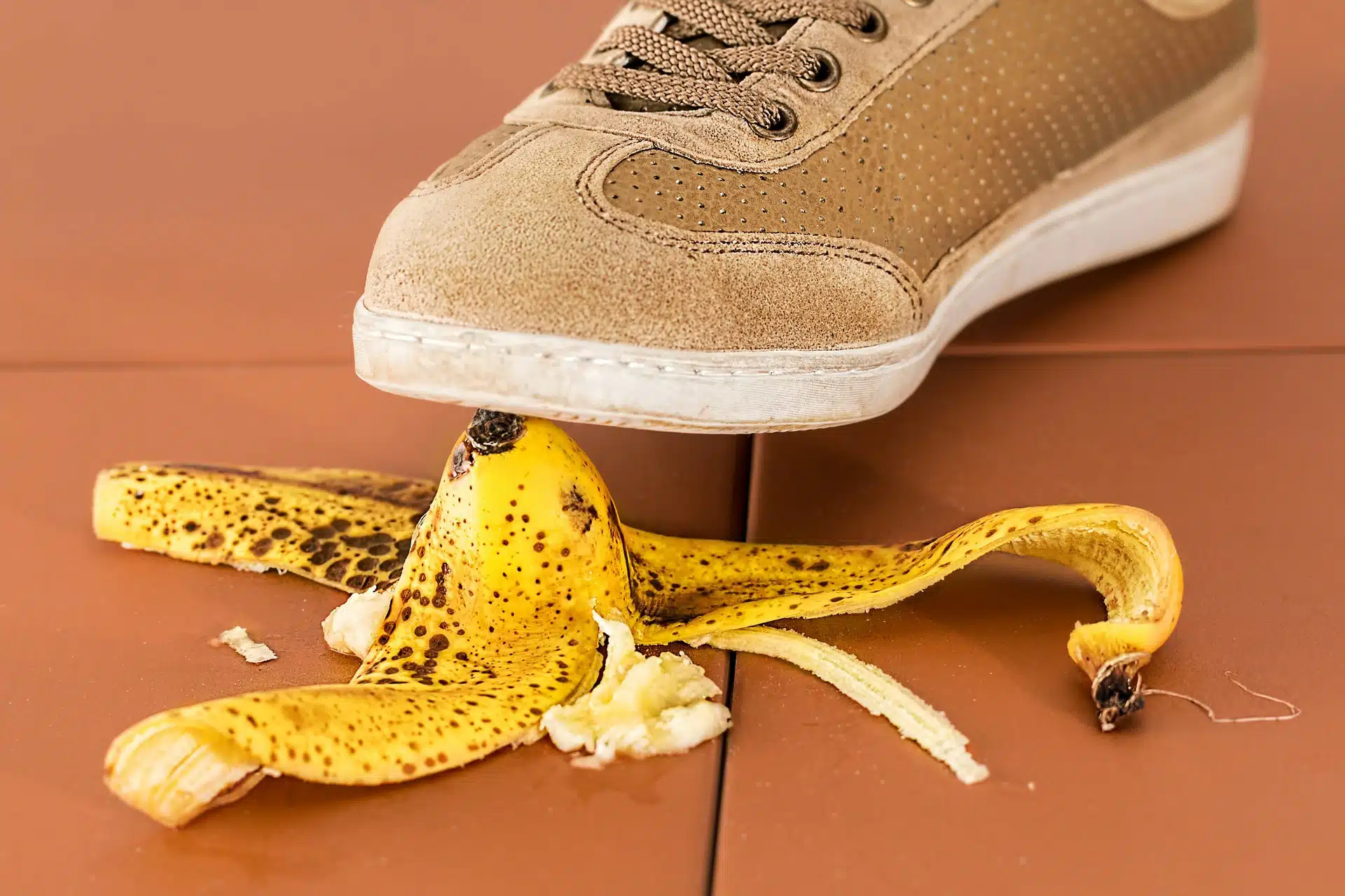 Beige shoe stepping on a banana peel spread on a brown tiled floor for business insurance article