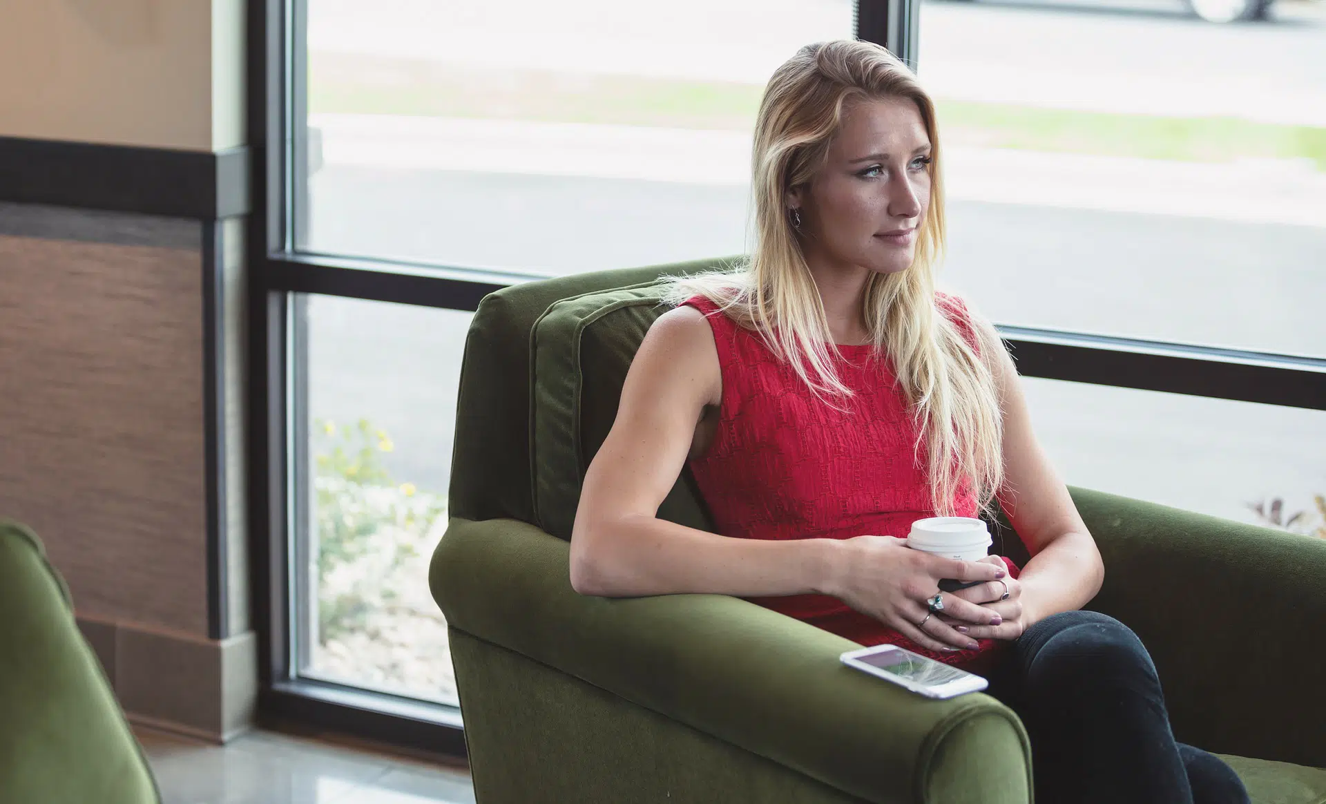 Woman in red dress sitting in armchair holding coffee by window illustrating hiring an apprentice article