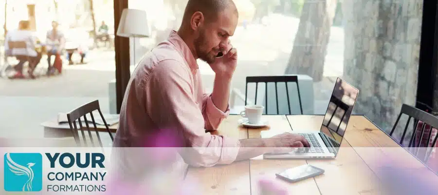 Man on phone using laptop at cafe table, illustrating How to Change the Person of Significant Control PSC Details article