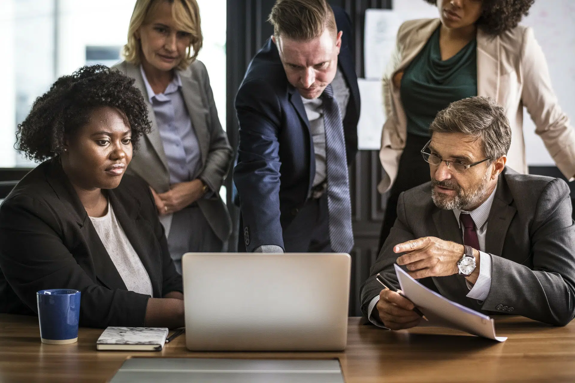 Team of five business professionals gathered around laptop reviewing documents for winning business marketing plan article