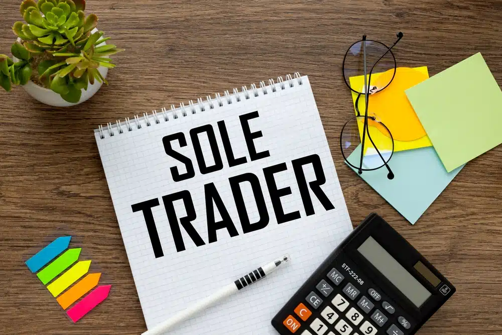 Notepad with Sole Trader written in bold text on a desk with a calculator and sticky notes representing how to register as a sole trader in the UK