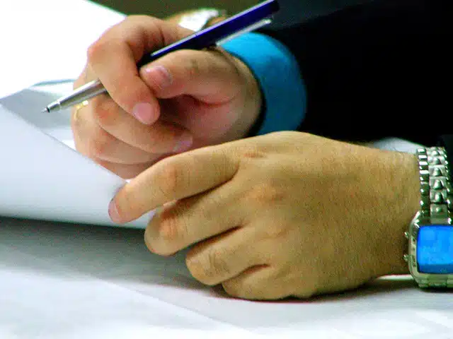 Hand holding pen writing on paper, illustrating written resolution article