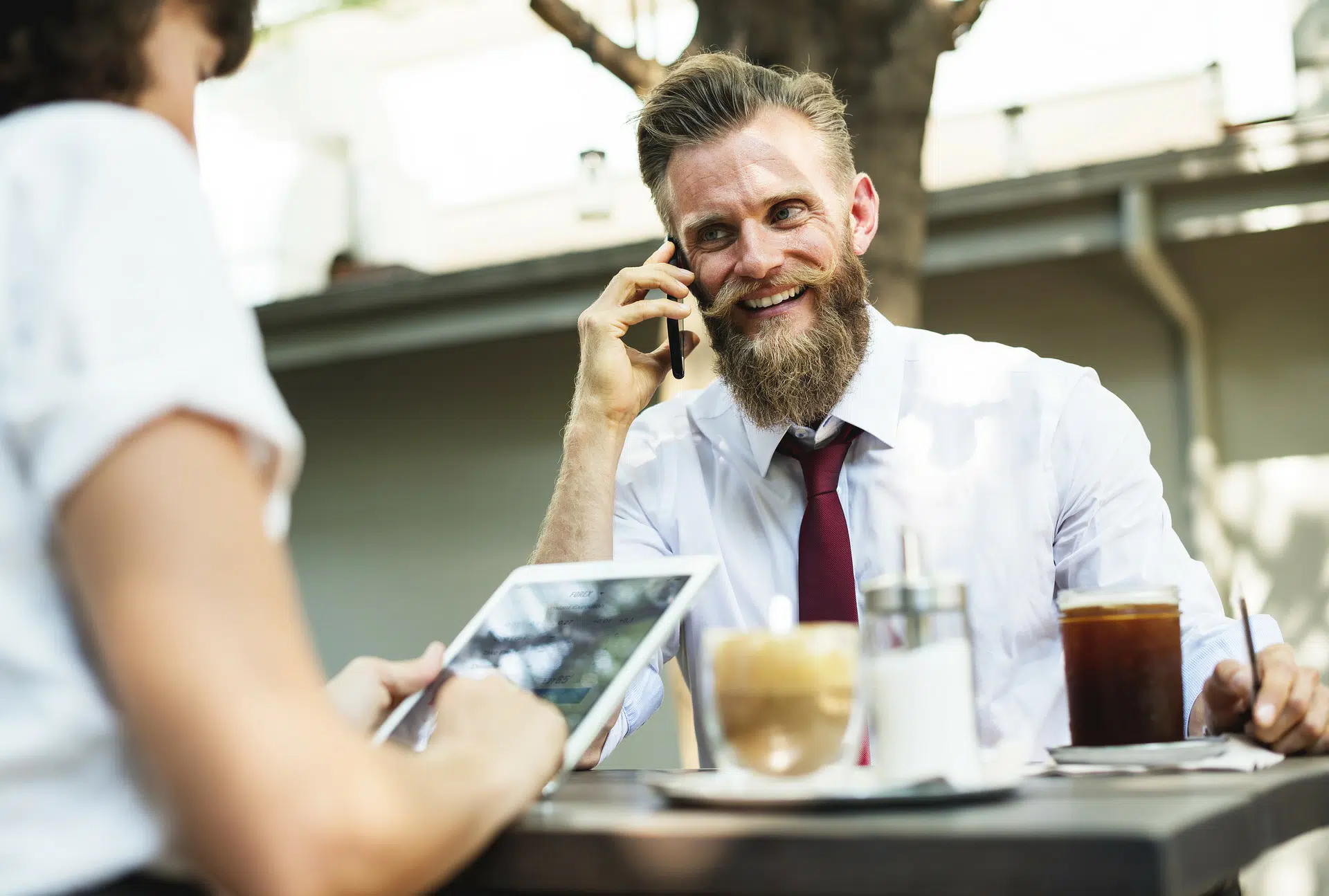 Bearded man on phone at café table with drinks and tablet illustrating Changes to Companies House PSC June 2017