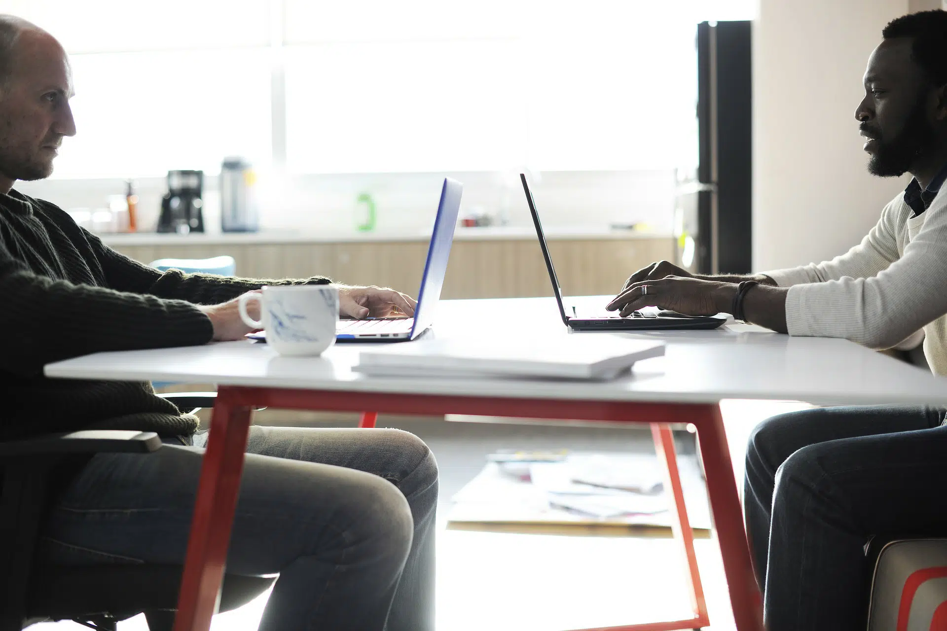 Two men facing each other working on laptops at table with coffee mug, illustrating impact of Article 50 on small businesses
