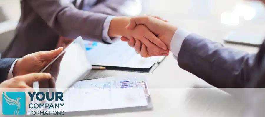 Two people shaking hands over documents and tablet, illustrating What Is a Shareholders Agreement business deal concept