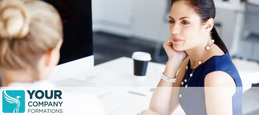 Two women in office conversation at desk with coffee, illustrating When a Limited Liability is a Smart Move decision scenario