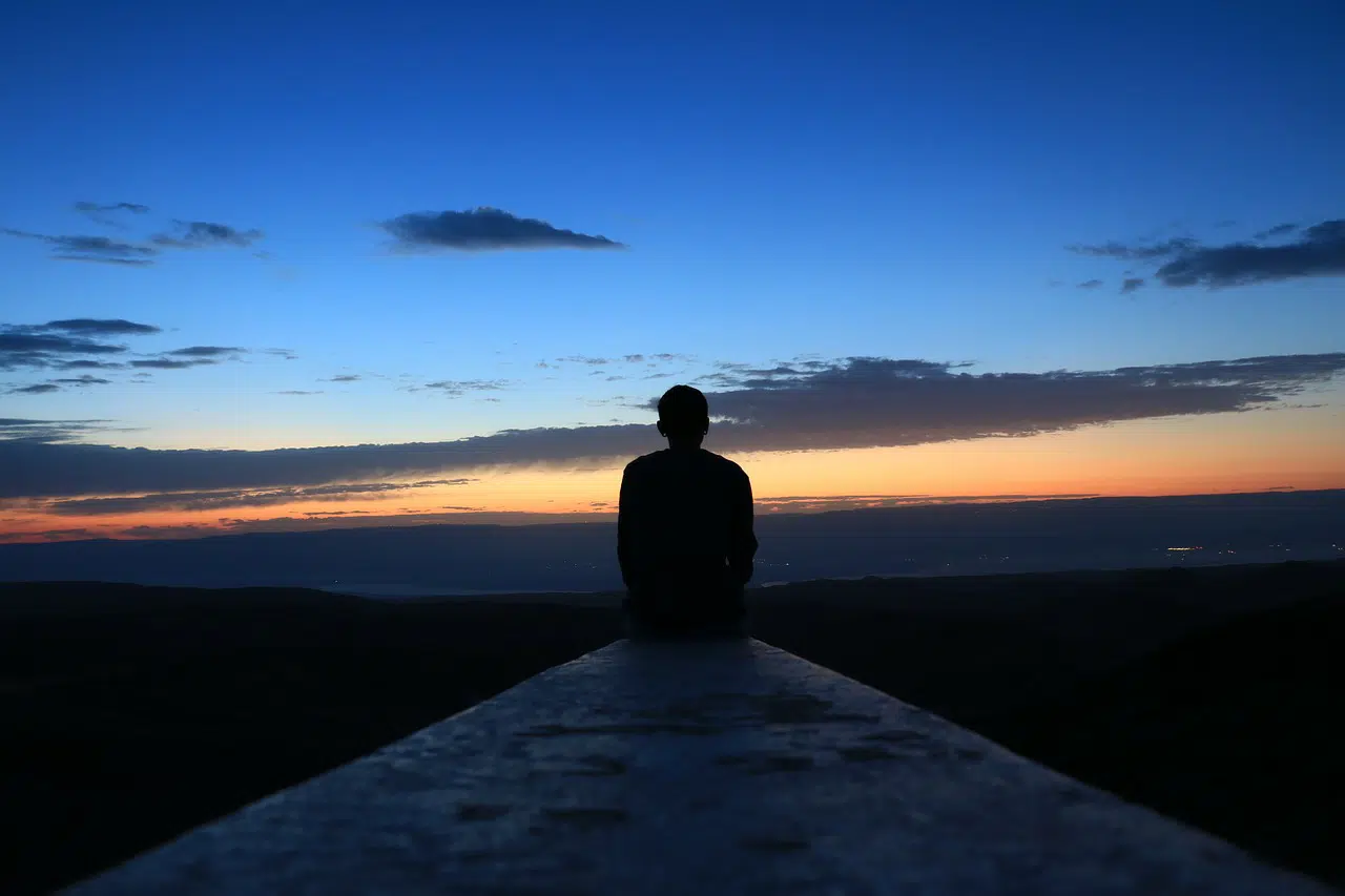 Silhouette of the back of a person sitting on ledge looking over the sky at sunset for sole trader or limited company article