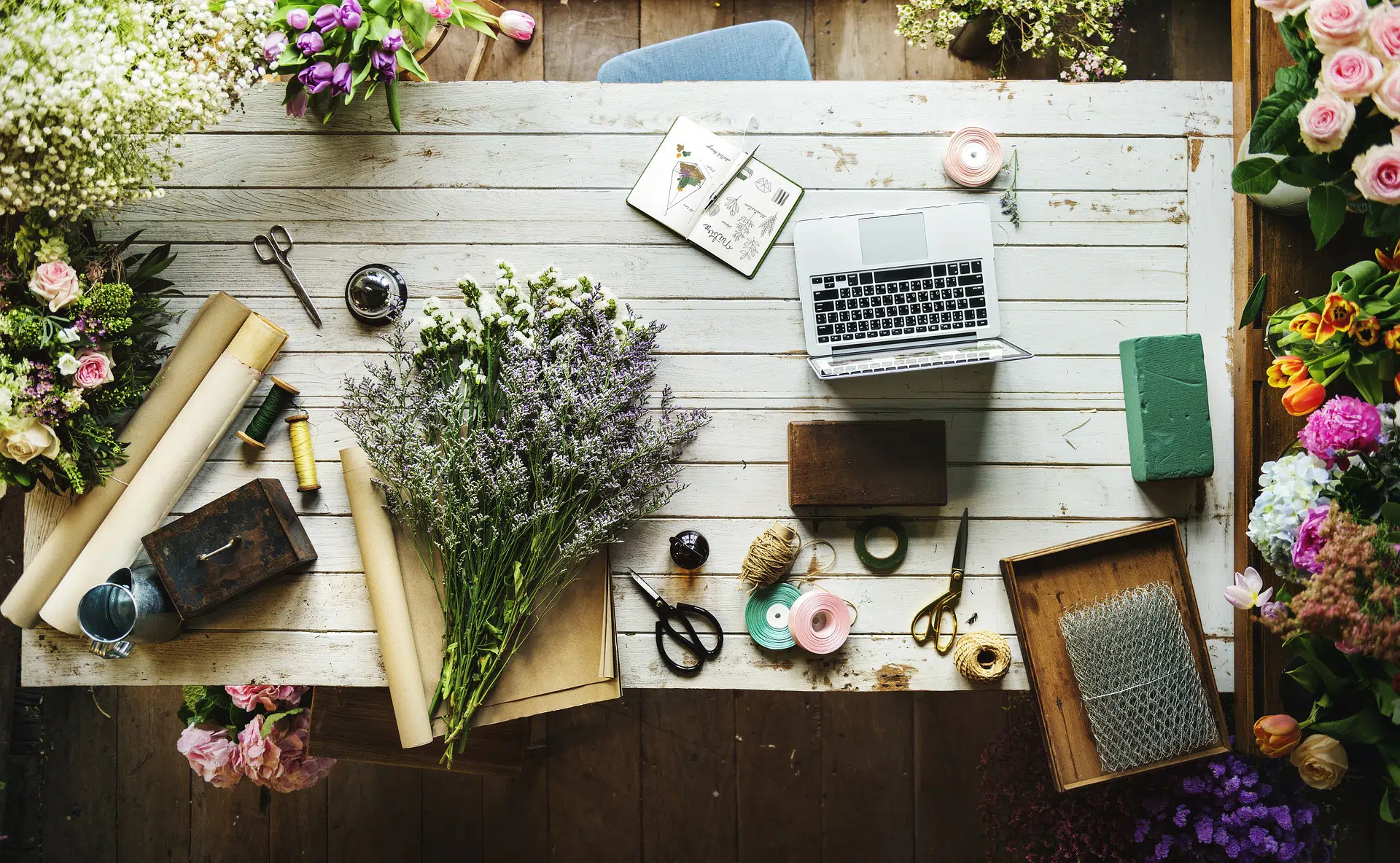 Overhead view of desk with laptop, flowers, scissors and tools illustrating why the Spring Budget was not good for SMEs
