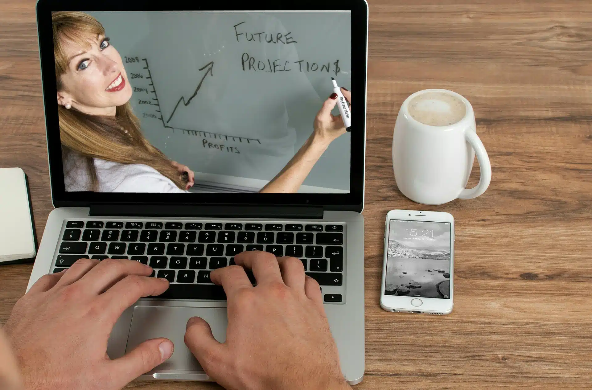 Hands typing on a laptop showing a woman drawing future projections beside coffee and a phone for “formed your company, what’s next” article
